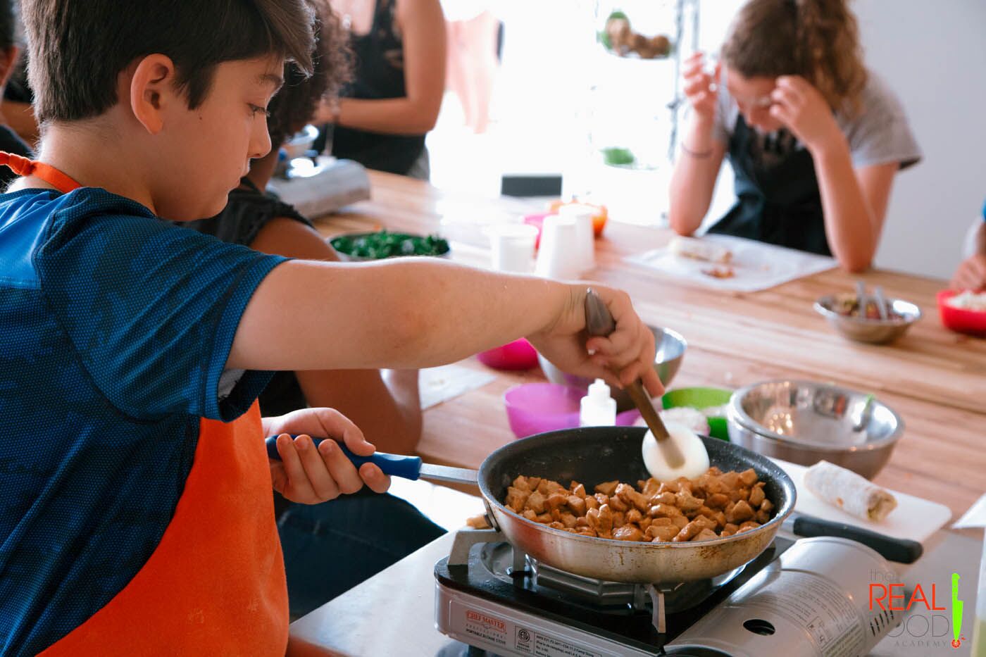 A little boy cooking fresh chicken at The Real Food Academy's cooking camp.