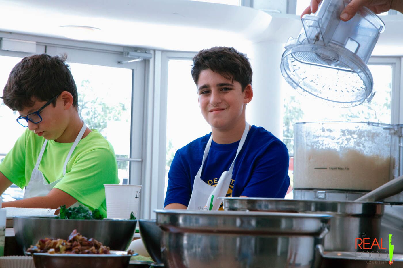 A young boy smiling in front of mixing bowls, check out our cooking classes for teens.