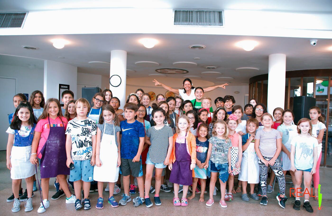 Chef Maria and a group of kids line up to take a photo during their kids cooking camp at The Real Food Academy!