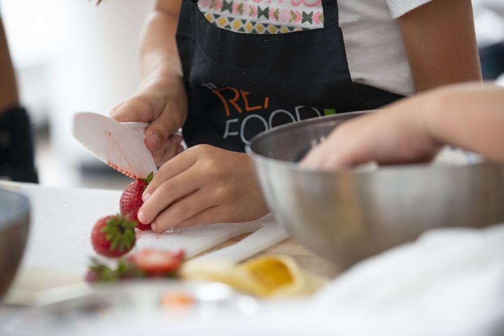 A child cutting a strawberry at The Real Food Academy cooking camp.