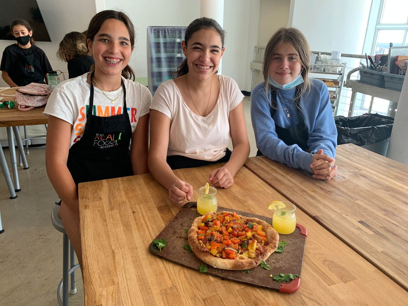 Three girls present a pizza made from wholesome ingredients at a teen The Real Food Academy cooking camp.