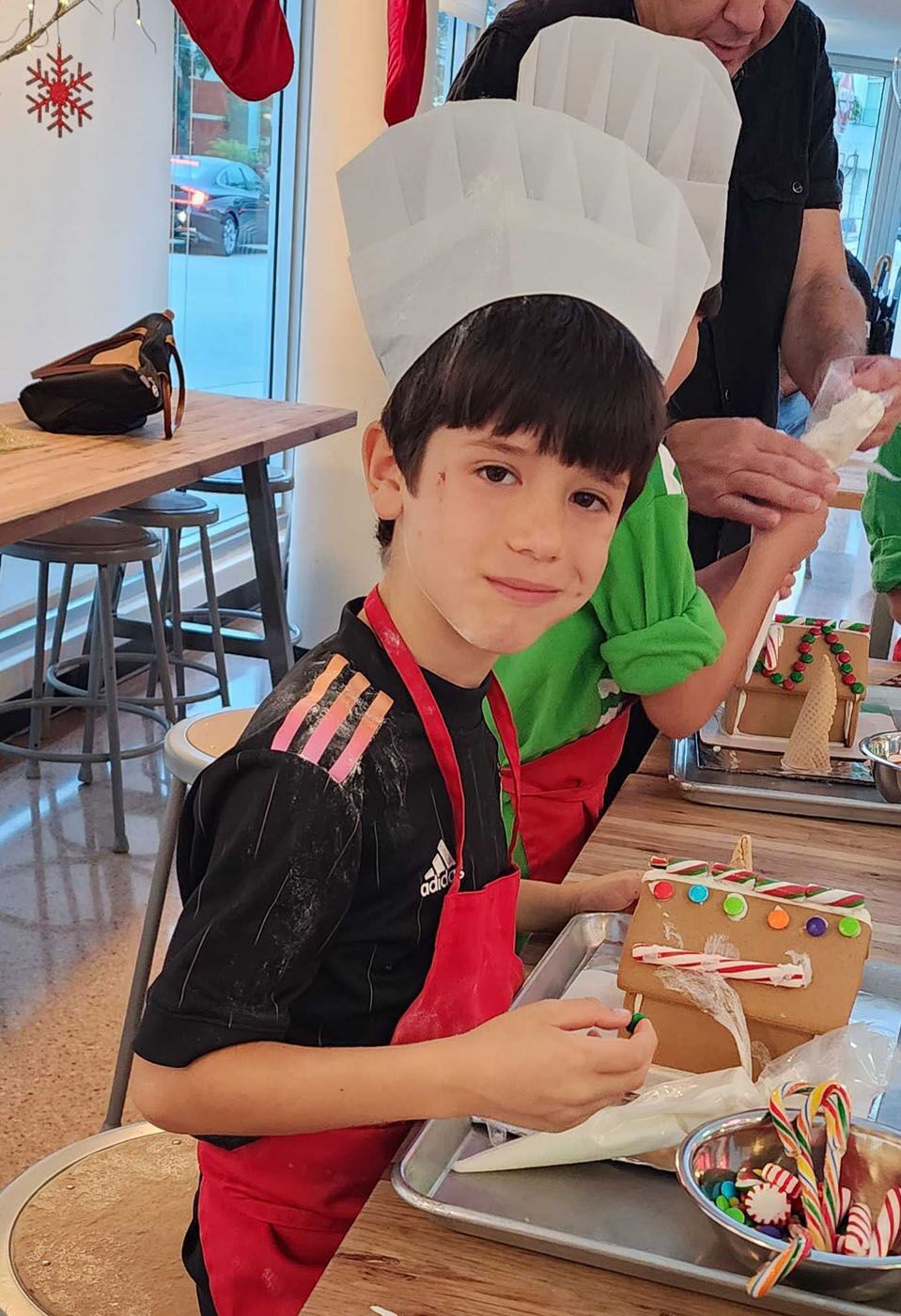 A young boy showing off his holiday creation at our gingerbread house class.