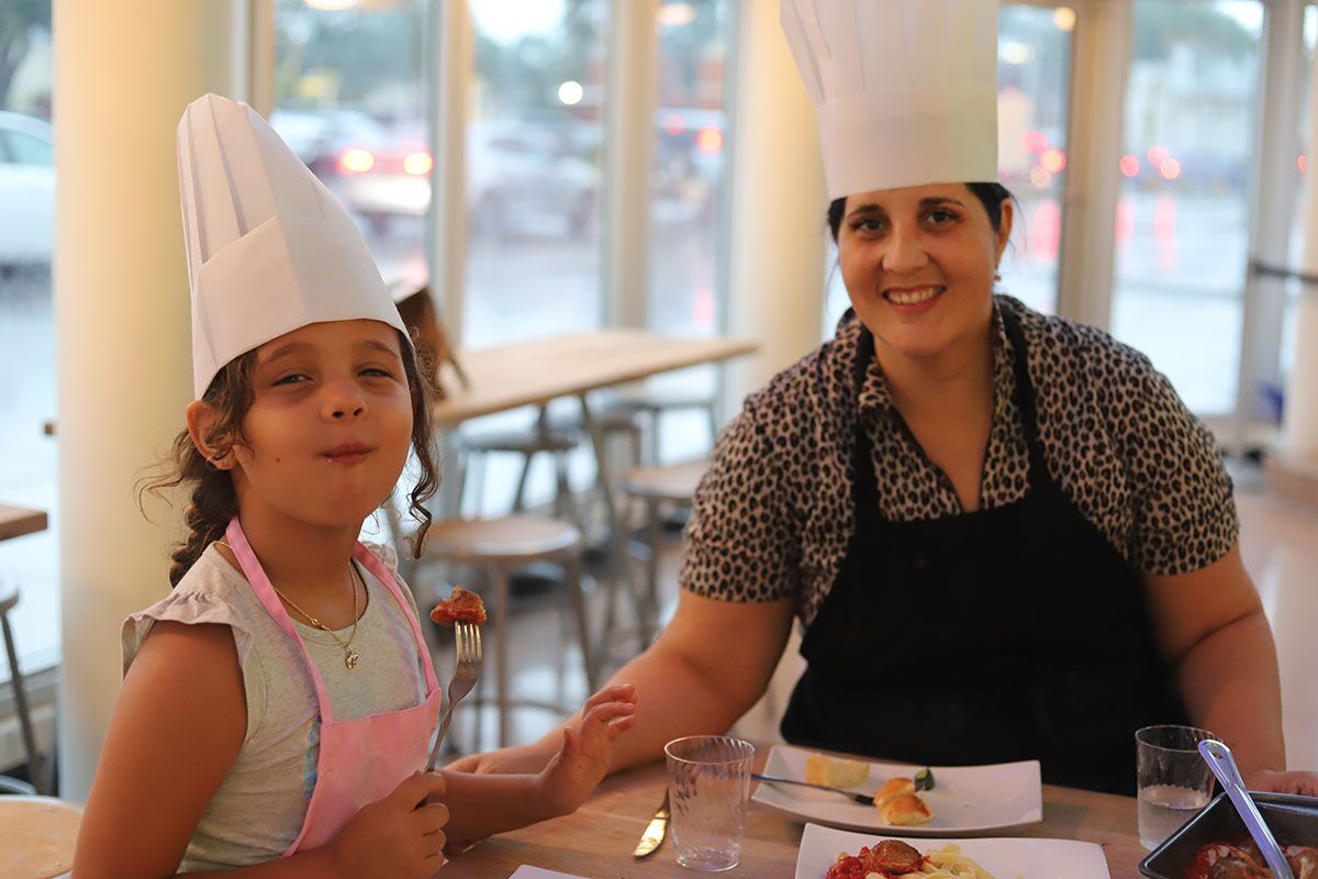A mom and daughter in red aprons smiling with a plate of food at The Real Food Academy.